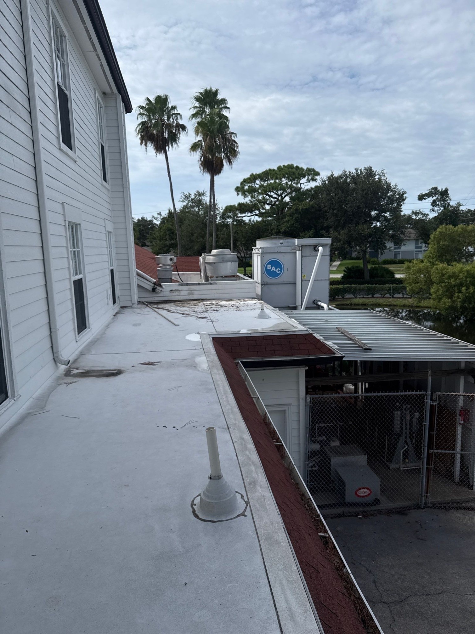 Low-slope roof section with a flashed pipe penetration and rooftop equipment beside a multi-story building