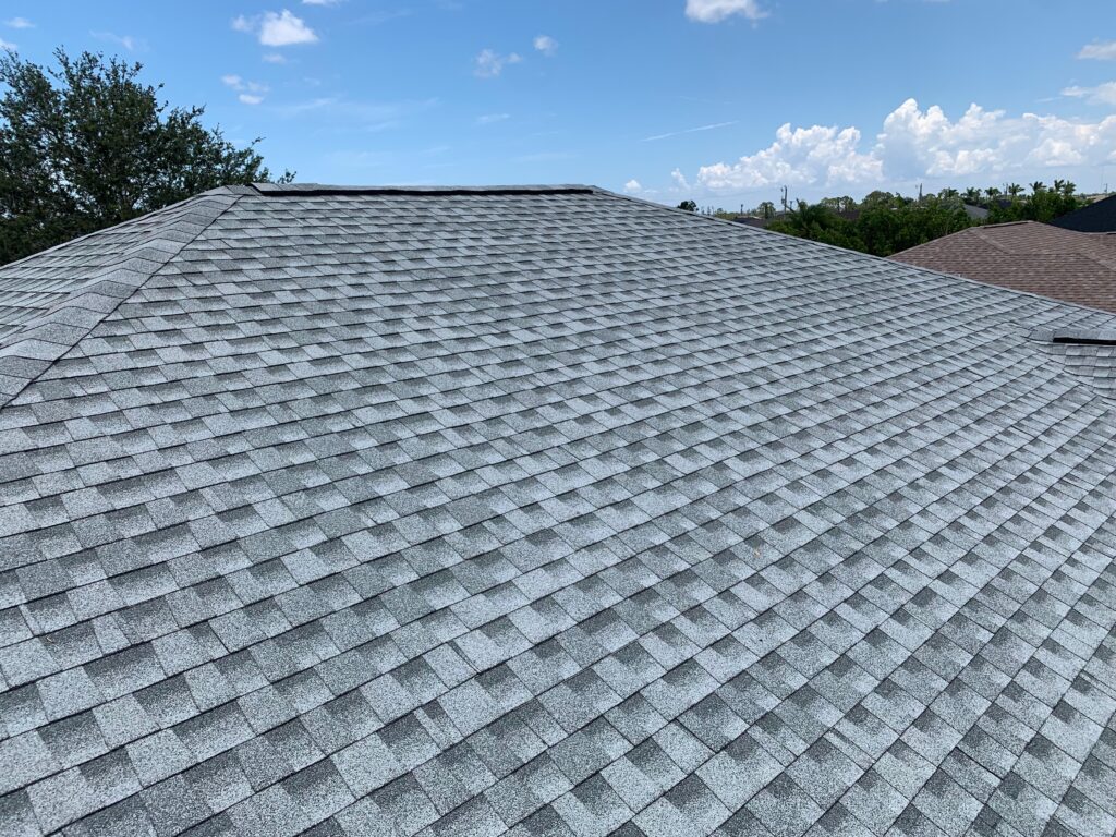 Completed gray architectural shingle roof with even courses under a blue sky