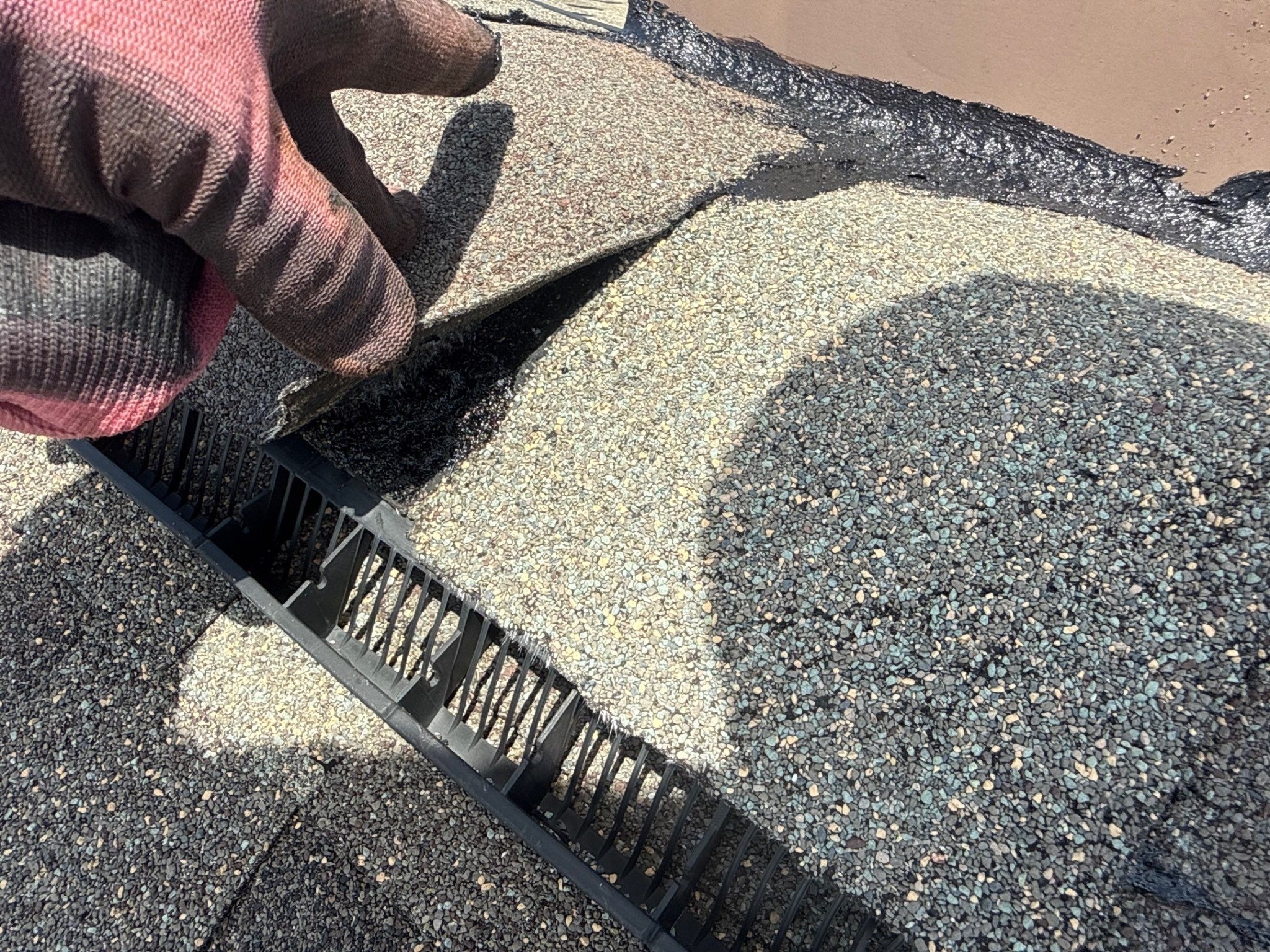 Gloved hand pointing to the baffle of a ridge vent along the ridge of a shingle roof