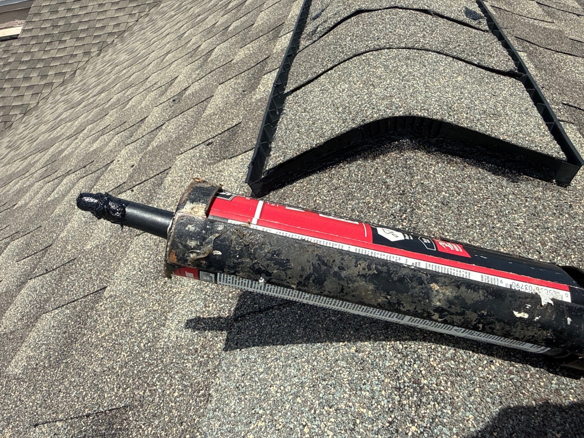 Ridge vent running along the ridge of an asphalt shingle roof with a sealant tube resting on the roof during a repair