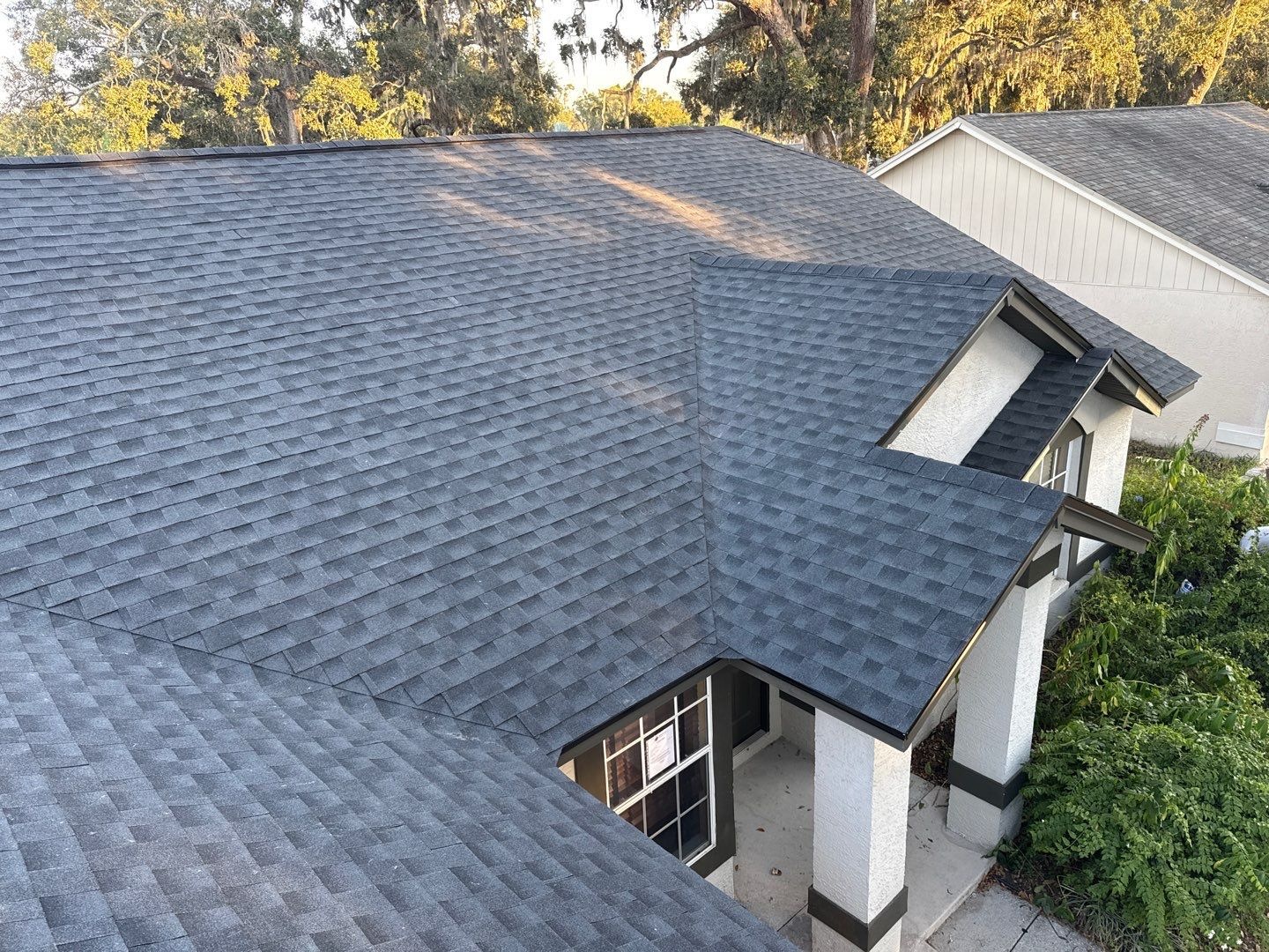 Aerial view of a newly installed gray architectural shingle roof with multiple hips and valleys, shown in late-afternoon light